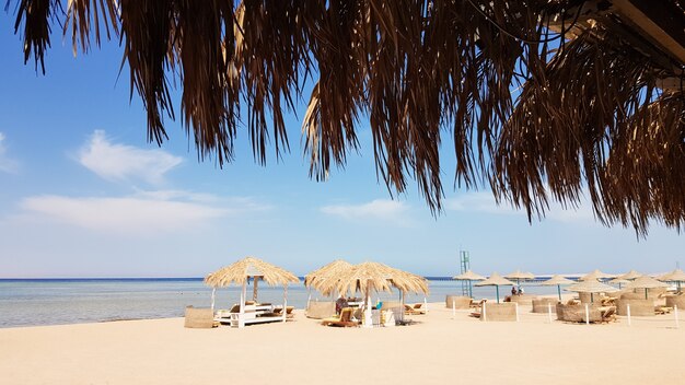 Una hermosa playa tropical con sombrillas de paja a orillas del Mar Rojo en Sharm El Sheikh. Paisaje de verano Hermosa playa soleada en Egipto. El concepto de vacaciones, viajes, vacaciones.