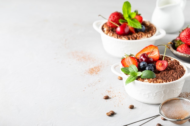 Una hermosa porción de postre tiramisú italiano, adornado con fresas, cerezas y menta sobre un fondo blanco. Copie el espacio para su texto.