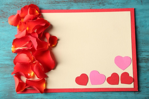 Hermosa postal hecha a mano con corazones de papel y pétalos de rosa sobre fondo de madera de color