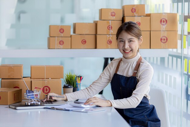 Una hermosa propietaria de un negocio asiático abre una tienda en línea y está revisando los pedidos de los clientes que envían productos a través de un concepto de empresa de mensajería de una mujer que abre un negocio en línea