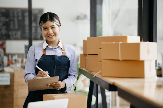 Una hermosa propietaria de un negocio asiático abre una tienda en línea y está revisando los pedidos de los clientes que envían productos a través de un concepto de empresa de mensajería de una mujer que abre un negocio en línea