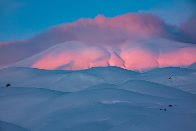 Hermosa puesta de sol de invierno en colinas nevadas con nubes de color rosa