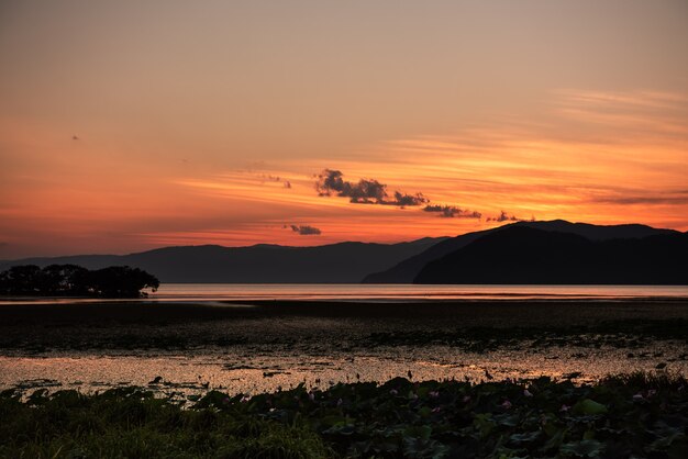 Hermosa puesta de sol en el lago Biwa, cielo anaranjado, montañas en silueta.