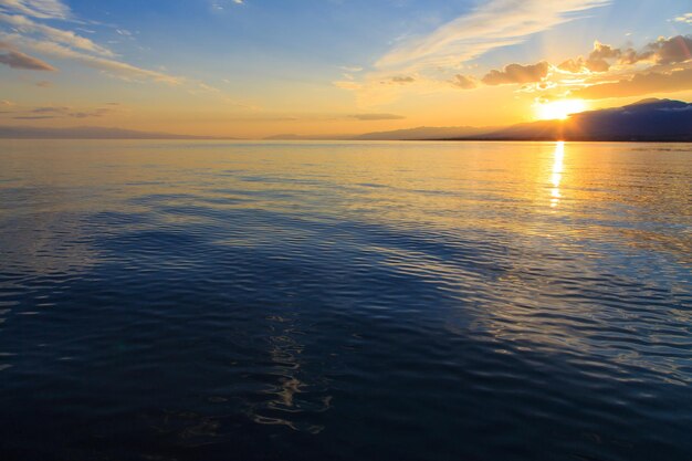 Hermosa puesta de sol nublada sobre el mar y las montañas Cielo brillante en los rayos del sol naranja natural