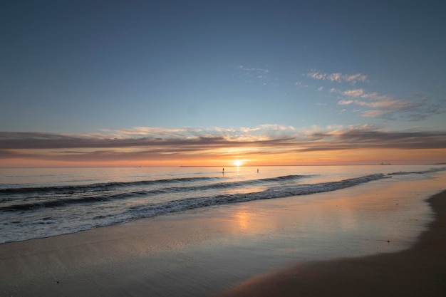 Una hermosa puesta de sol en la playa de Mazagón España En el fondo las siluetas de dos surfistas