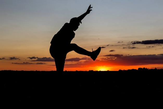 Foto hermosa puesta de sol con silueta de niño saltando de alegría