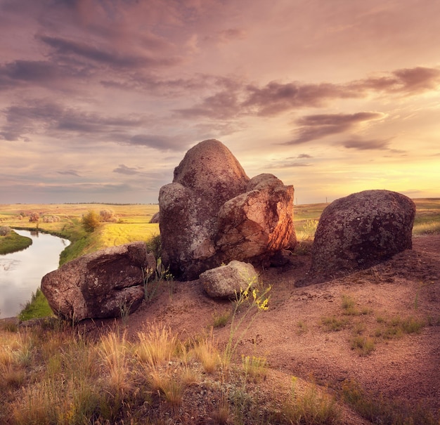 Hermosa puesta de sol de verano en el río con piedras antiguas