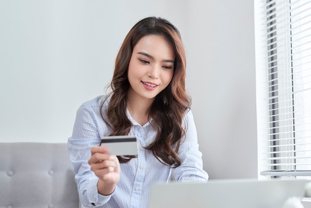 Una hermosa que usa una computadora portátil y su tarjeta bancaria mientras compra desde casa sin un sofá.
