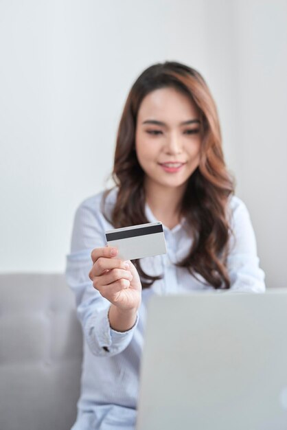 Una hermosa que usa una computadora portátil y su tarjeta bancaria mientras compra desde casa sin un sofá.