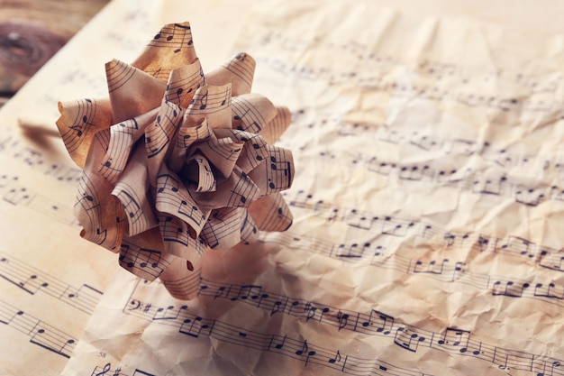 Foto hermosa rosa hecha en papel en el fondo de la página de notas musicales
