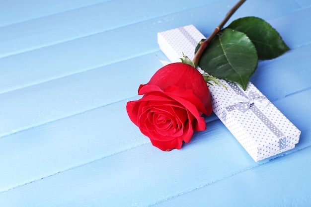 Hermosa rosa roja con caja de regalo sobre fondo de tablones de madera de color