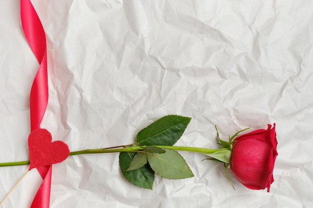 Hermosa rosa roja con cinta y corazón en un palo en el fondo en papel arrugado. Vista superior. Copia espacio