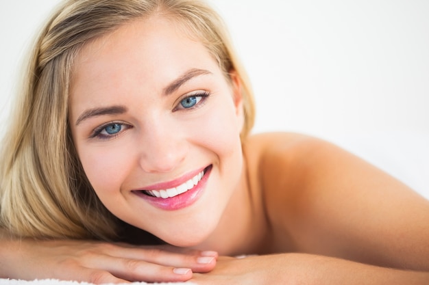 Hermosa rubia acostada en la mesa de masaje sonriendo a la cámara