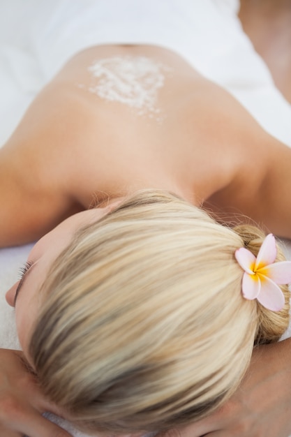 Hermosa rubia acostada en la mesa de masaje con tratamiento de exfoliación