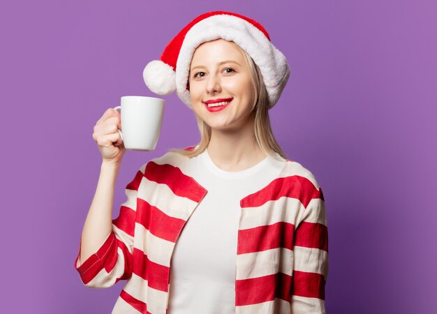 Hermosa rubia en chaqueta roja y sombrero de Navidad sobre fondo púrpura