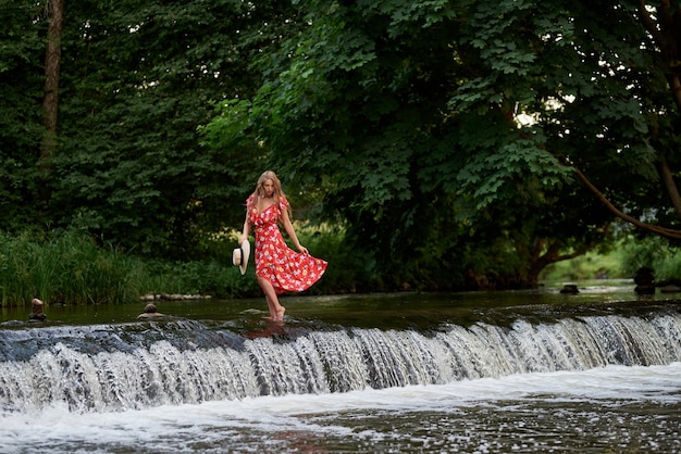 Hermosa rubia feliz con un vestido de verano y un sombrero de paja se encuentra en el agua