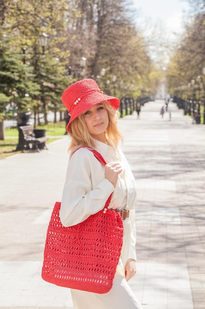 Hermosa rubia en un paseo con una bolsa y un sombrero rojo hecho a mano