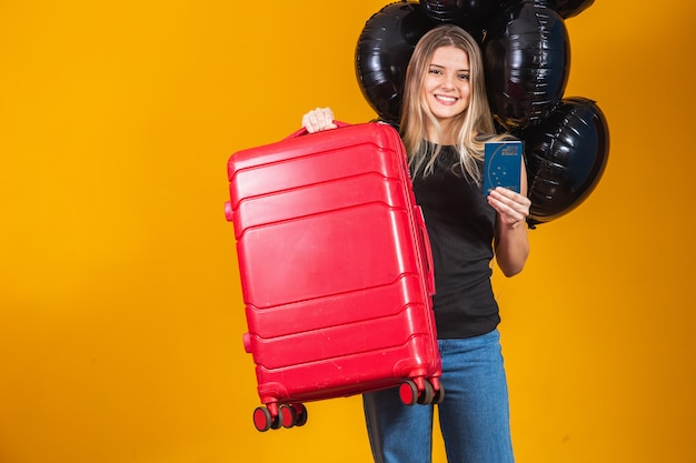 Hermosa rubia de pelo lacio en viaje. Próximo viaje. Chica sosteniendo pasaporte brasileño. Sobre fondo amarillo. viajes de viernes negro