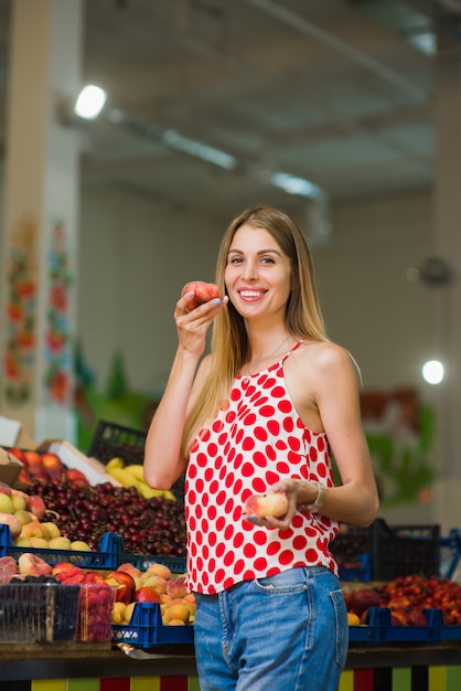 Hermosa rubia posando con duraznos en el mercado