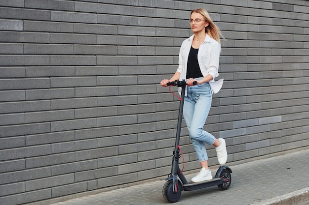 Hermosa rubia con ropa informal montando una escotilla eléctrica al aire libre durante el día soleado