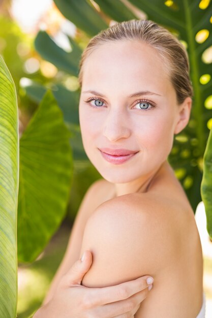 Hermosa rubia sonriendo a la cámara detrás de la hoja