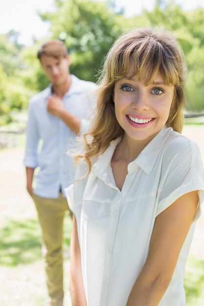 Hermosa rubia sonriendo a la cámara con novio en segundo plano