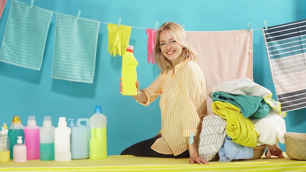 Hermosa rubia sonriente publicidad de detergentes profesionales en una pared azul aislada