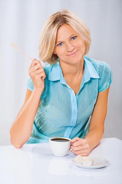 Hermosa rubia sosteniendo palo de azúcar y taza de café