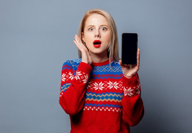Hermosa rubia en suéter de Navidad con teléfono móvil en gris