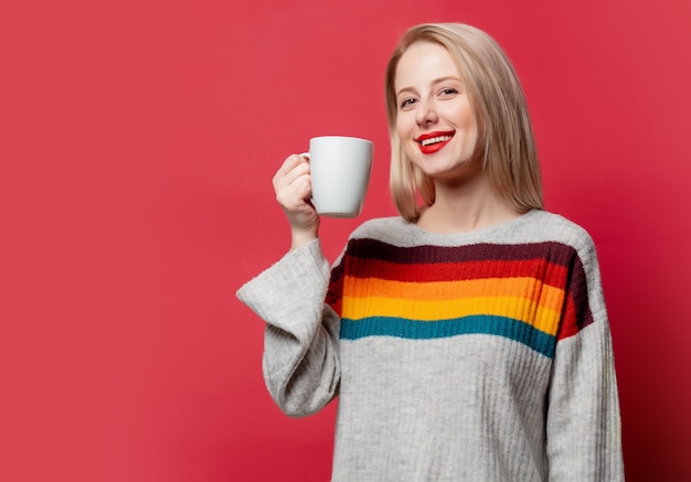 Hermosa rubia en suéter con taza de café en rojo