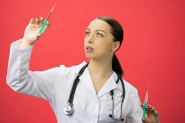 Hermosa sexy médico de laboratorio compara las inyecciones, levanta la jeringa y la mira