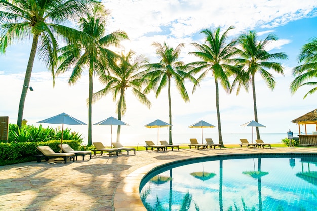 Hermosa sombrilla de lujo y una silla alrededor de la piscina al aire libre en el hotel y resort con palmera de coco en el cielo azul - concepto de vacaciones y vacaciones