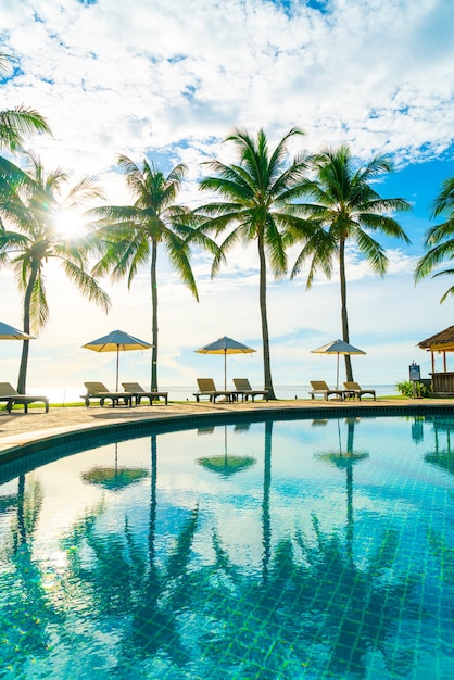 Hermosa sombrilla de lujo y una silla alrededor de la piscina al aire libre en el hotel y resort con palmera de coco en el cielo azul - concepto de vacaciones y vacaciones