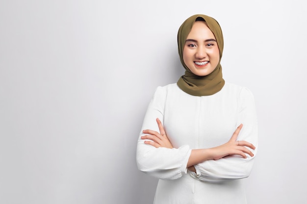 Hermosa sonriente amigable joven árabe asiática musulmana con hiyab de pie con los brazos cruzados y mirando a la cámara aislada sobre fondo blanco Concepto de estilo de vida religioso de la gente