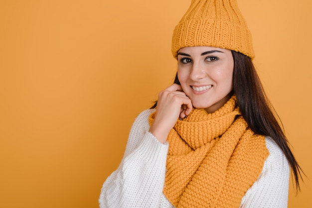 Foto hermosa y sonriente niña en un gorro de punto y con una bufanda posa maravillosamente en el estudio