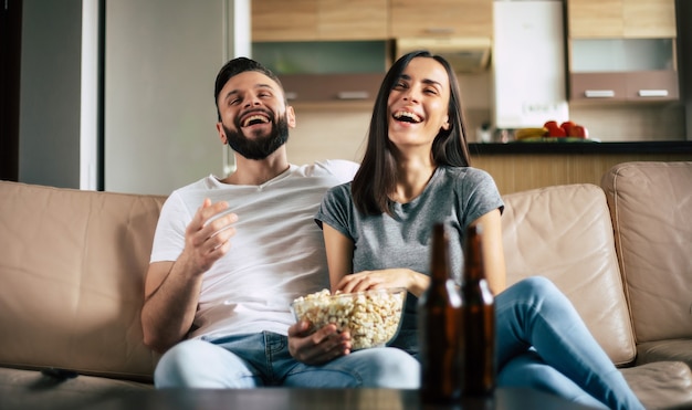 Hermosa y sonriente pareja moderna enamorada está viendo una película o una película en la televisión mientras se relajan en el sofá de su propio apartamento