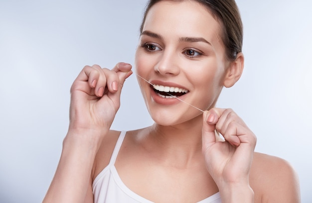 Hermosa sonrisa, dientes blancos y fuertes. Cabeza y hombros de mujer con sonrisa blanca como la nieve sosteniendo hilo dental, concepto estomatológico. Chica limpiando los dientes con hilo