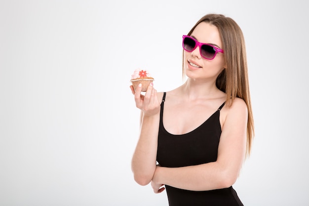 Hermosa sonrisa feliz contenido alegre chica atractiva en gafas de sol rosa sosteniendo un cupcake en sus manos