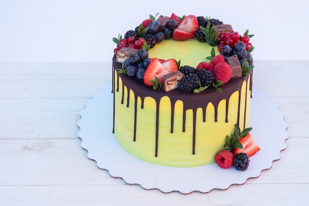 Hermosa tarta de cumpleaños casera con crema blanca, glaseado de chocolate y bayas frescas naturales sobre fondo blanco.