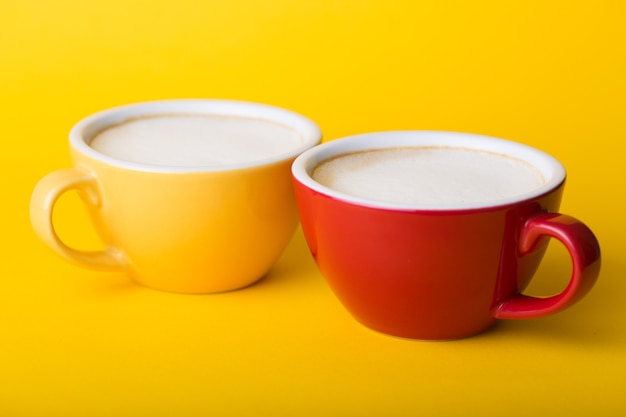 Foto hermosa taza de café amarillo y rojo con capuchino sobre fondo amarillo