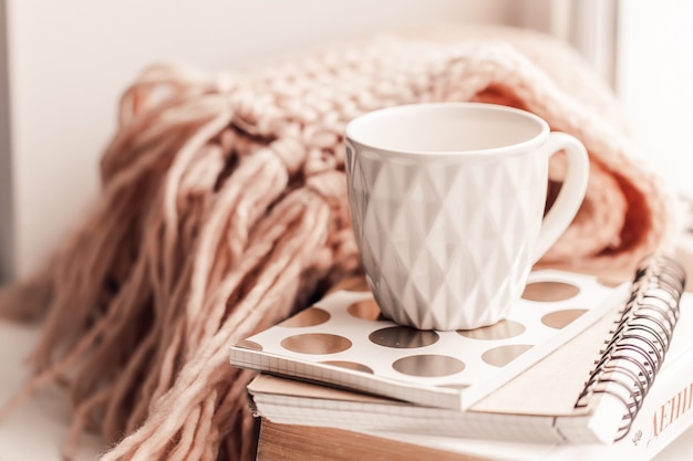 Hermosa taza rosa de té con cuaderno y bufanda tejida