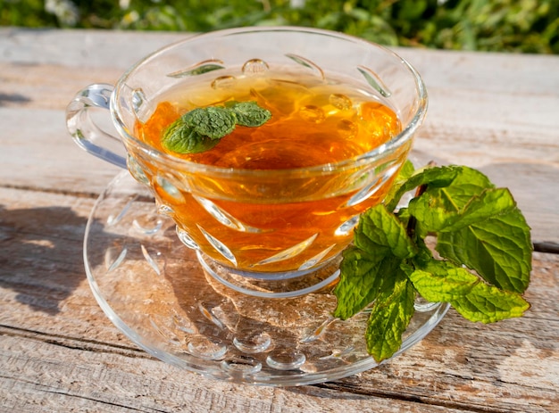 Hermosa taza de vidrio con té de menta en una mesa de madera del sol poniente en Grecia