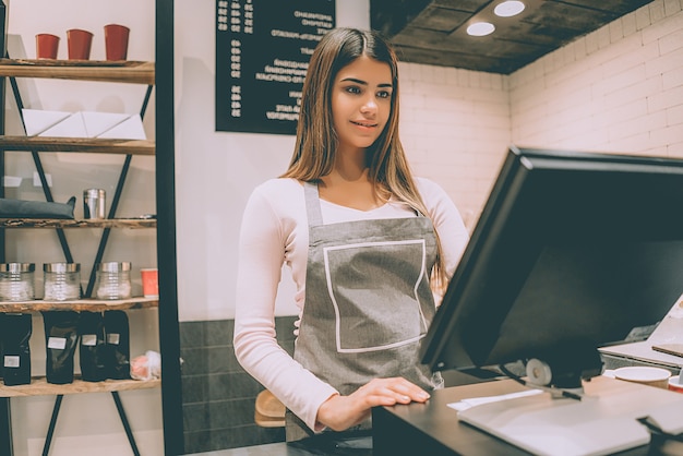 La hermosa trabajadora de la cafetería de pie detrás de la caja registradora