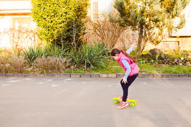 Hermosa y valiente patinadora en edad escolar entrenando para andar en una tabla amarilla al aire libre en primavera Primeros pasos de andar en patineta