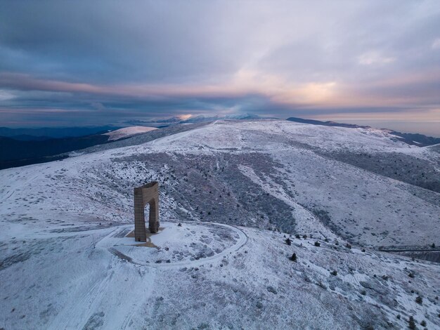 Hermosa vista aérea de las montañas cubiertas de nieve y el Arco del Monumento a la Libertad en la cresta principal de las Montañas Balcánicas de Bulgaria en la mañana de invierno