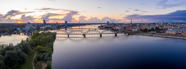 Hermosa vista aérea de la orilla del río Daugava en Riga, Letonia al atardecer. Volando sobre Riga con el puente de hierro del tren que cruza el río.