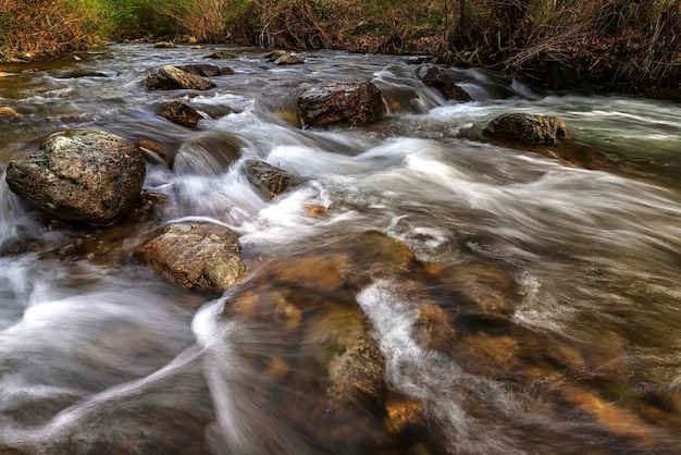 Hermosa vista de desenfoque de movimiento del agua que fluye en el río con piedras