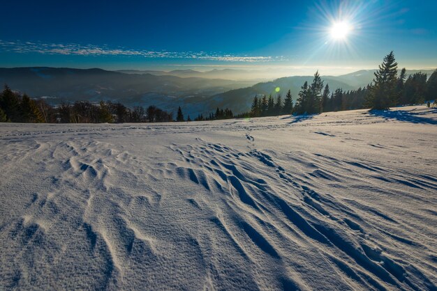 Hermosa vista fascinante de las olas de nieve de esquí con vistas al bosque de coníferas y las cadenas montañosas en un soleado día de invierno helado. Concepto de vacaciones de esquí. Espacio publicitario