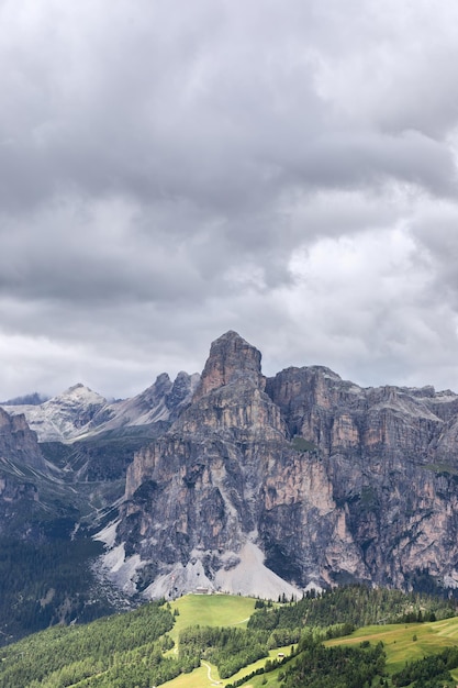 Hermosa vista de la montaña Sassongher con nubes de lluvia baja y un prado iluminado por el sol al pie