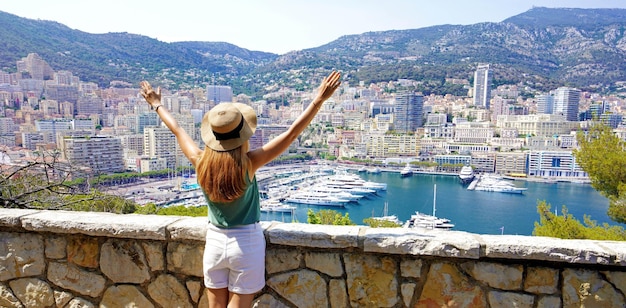 Hermosa vista panorámica de una mujer joven levantando los brazos en el paisaje urbano y el puerto deportivo de Montecarlo en Mónaco